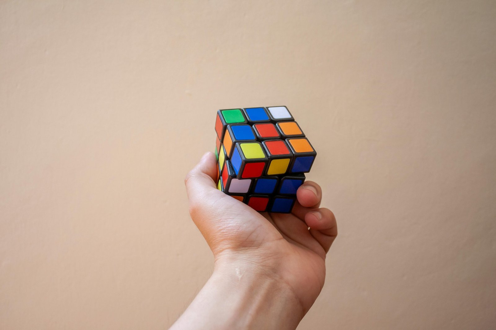 Close-up of a hand holding a colorful Rubik's Cube against a neutral background.